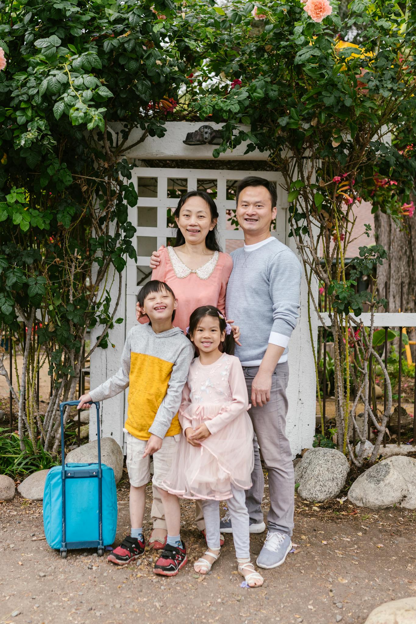 A cheerful family of four posing together outdoors in a lush garden setting.