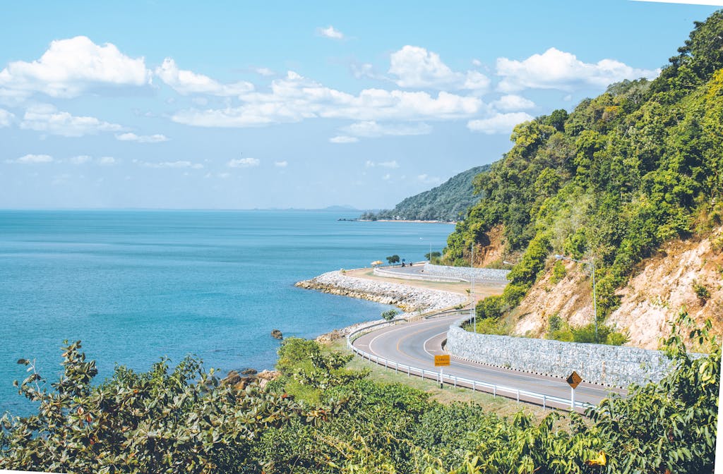 A stunning view of a winding coastal road alongside lush green hills and a vibrant blue ocean under a clear sky.