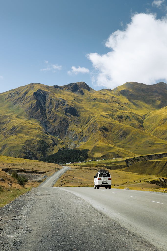 A white car travels through a stunning mountainous landscape under a bright blue sky, perfect for adventure and travel themes.