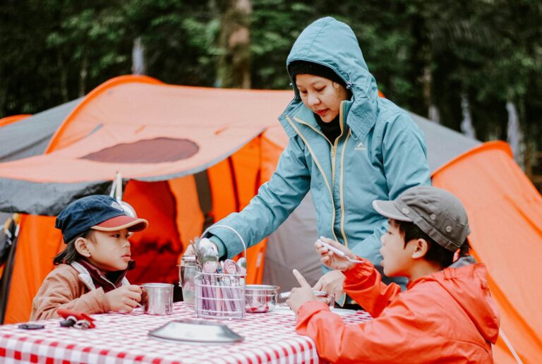 Mother serving food to her children at a campsite with orange tents in the background.
